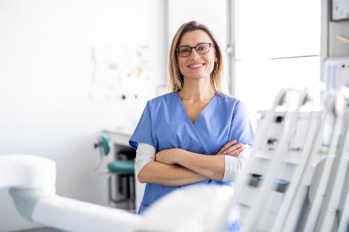 female dental professional standing next to dental chair and smiling