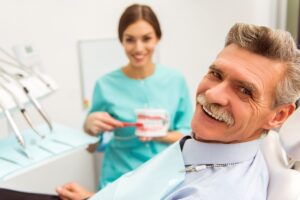 Man smiling broadly in dental chair discussing foods to avoid with dentures with hygienist