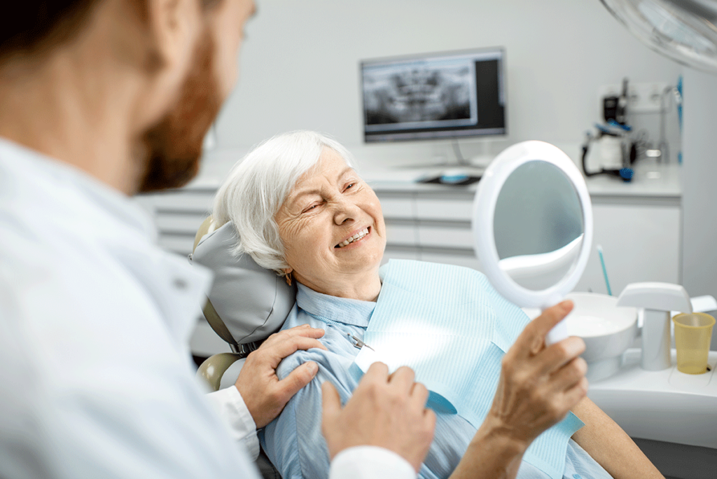 image of older woman in dental chair looking at smile in a mirror asking what is the difference between full and partial dentures