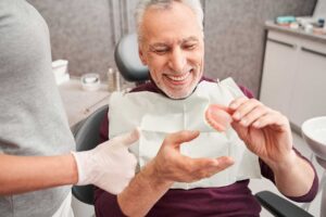 Smiling man holding model of dentures while learning about the cost of denture treatments