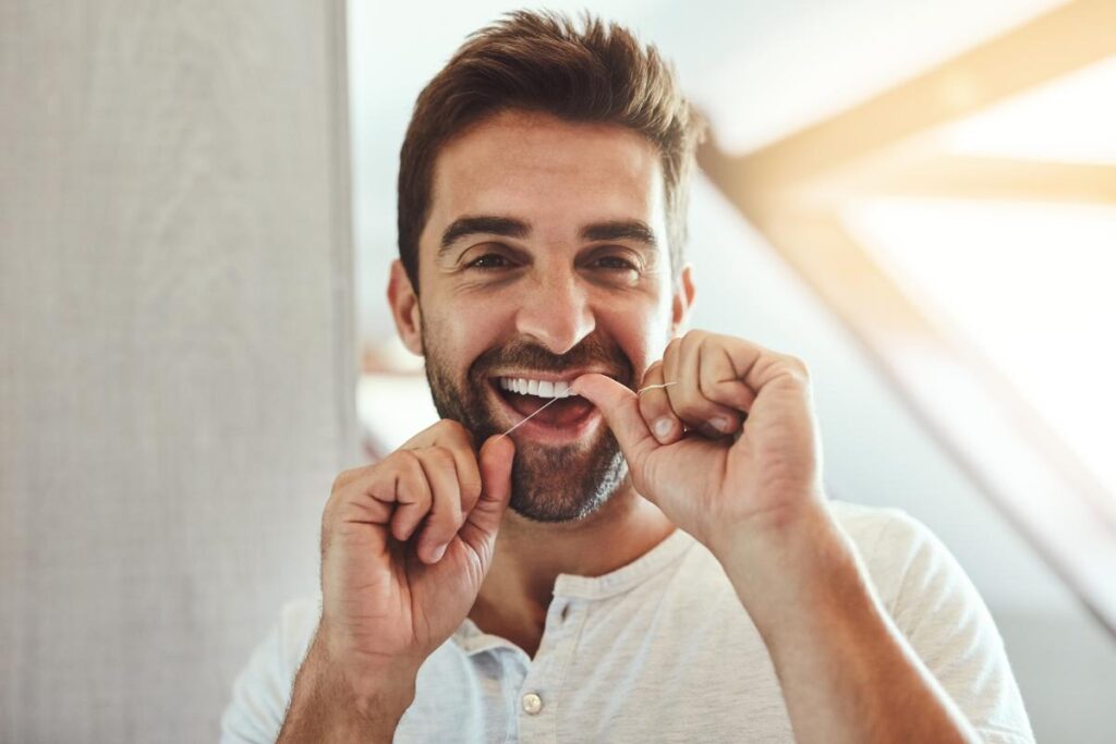 Person smiling while flossing to keep teeth healthy and beautiful after receiving pro bono dental care